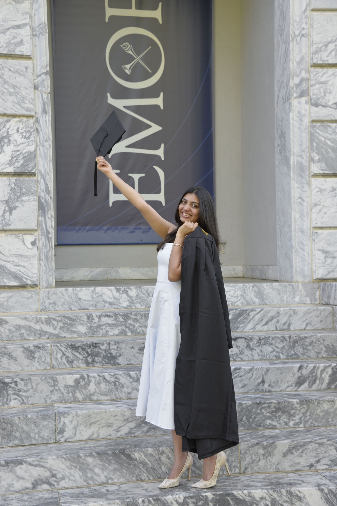 Anushka tossing her graduation cap in front of an Emory University banner